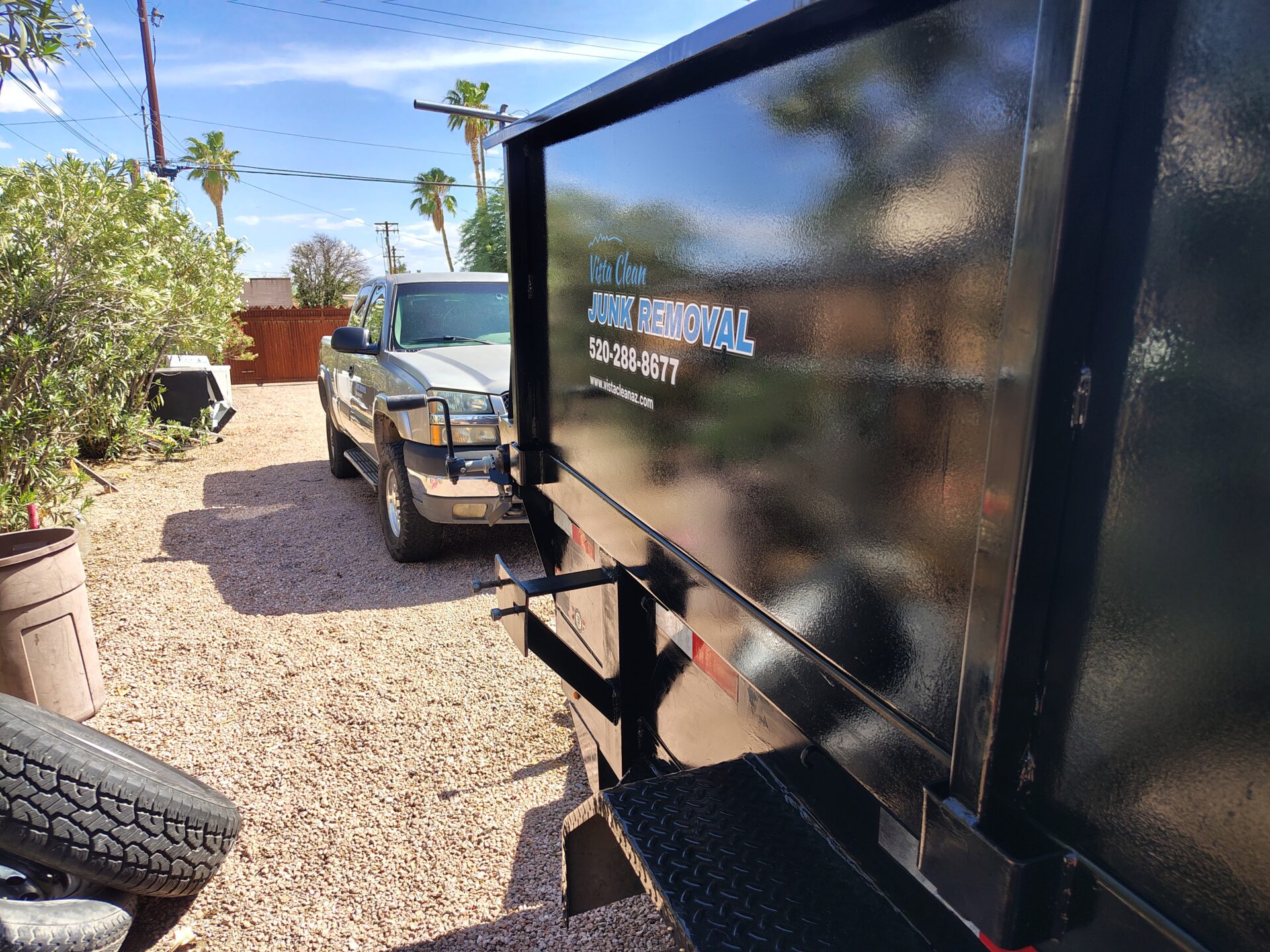 A picture of a vista clean junk removal truck and trailer on a property with bushes and trees in the background